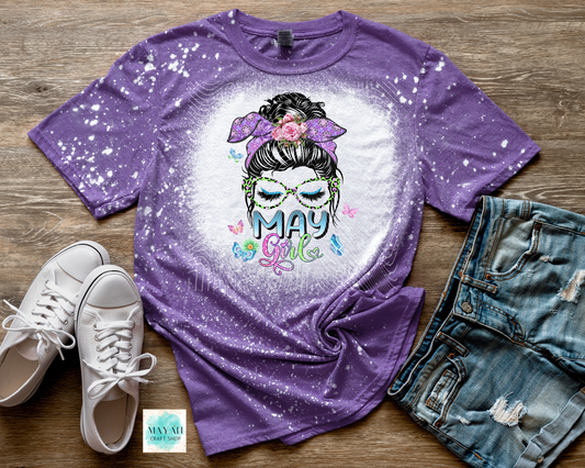 Purple t-shirt with 'May Girl' design on a wooden surface with shoes and jeans.