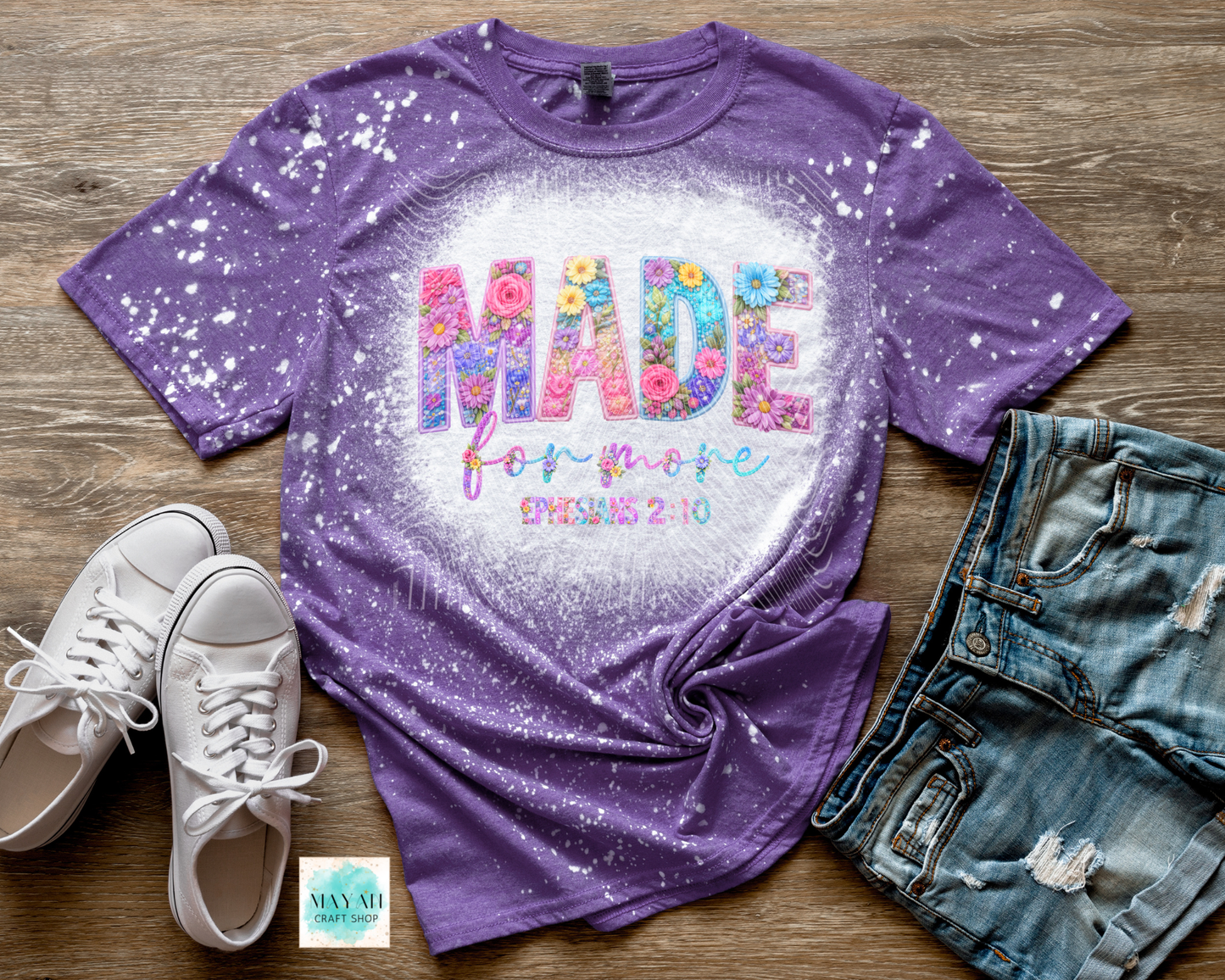 Purple t-shirt with colorful text design on a wooden surface with shoes and jeans.