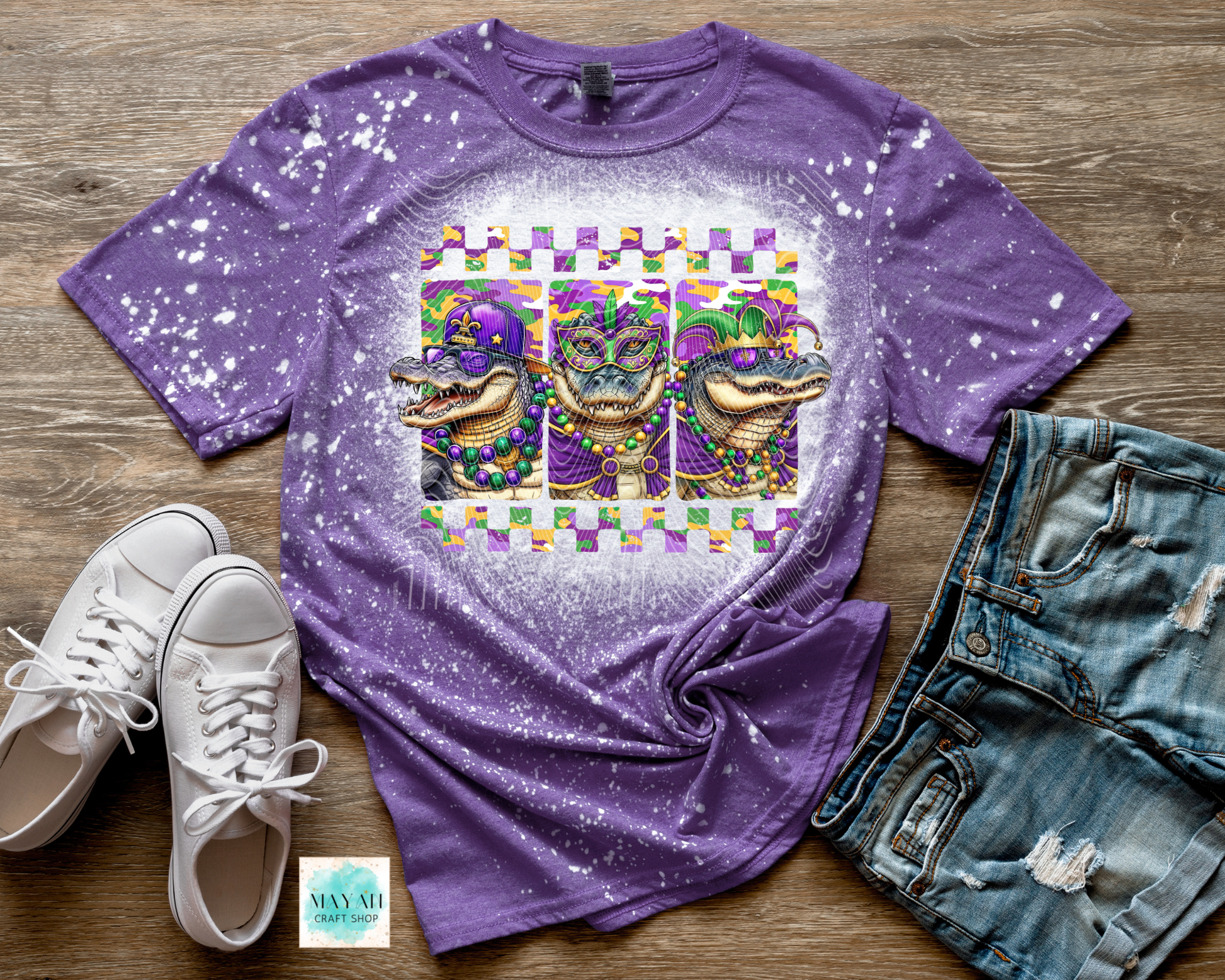 Purple t-shirt with Mardi Gras-themed design featuring alligators on a wooden surface with white sneakers and denim shorts.
