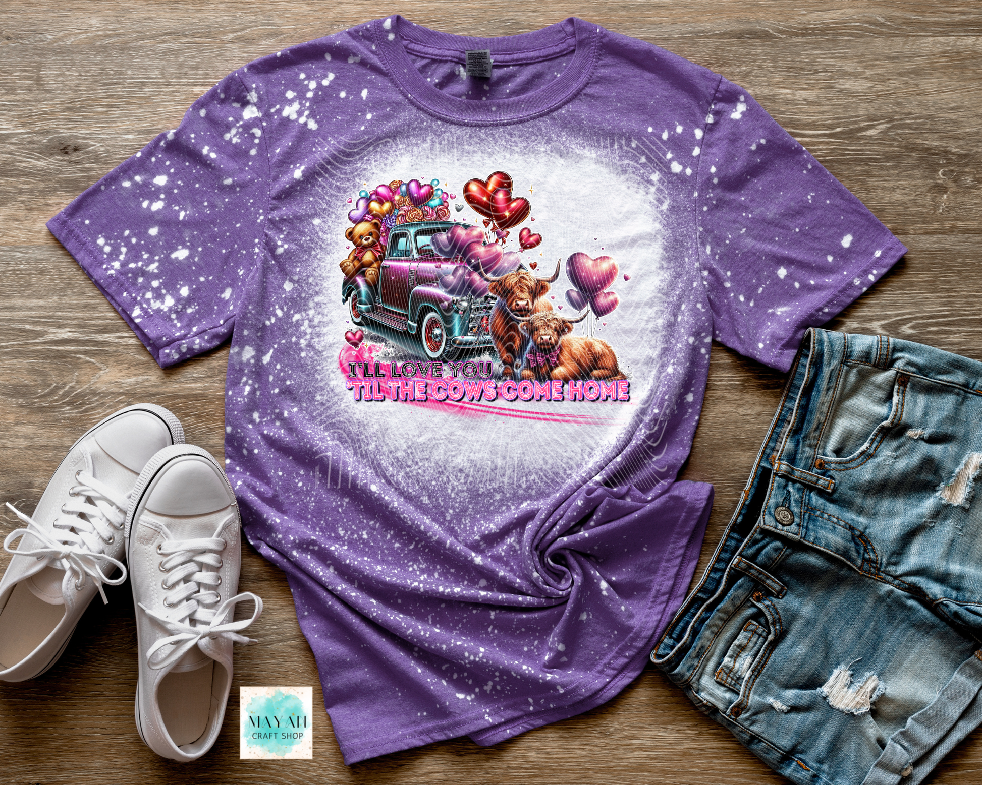 Purple t-shirt with graphic design of a pink truck and cartoon characters on a wooden surface with white sneakers and denim shorts.