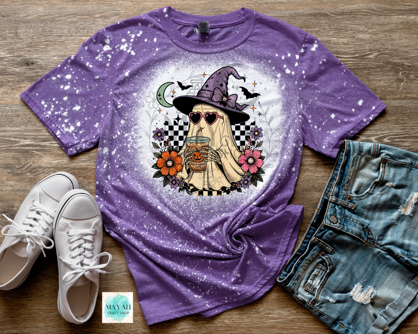 Purple t-shirt with a ghost graphic on a wooden surface with shoes and shorts.