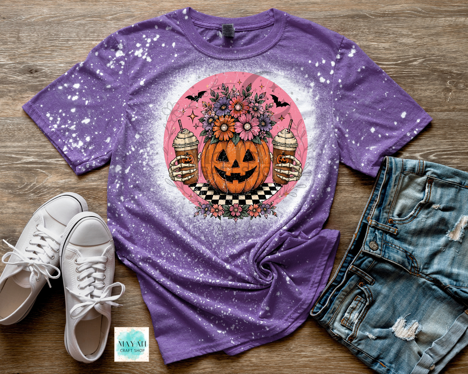 Purple t-shirt with Halloween-themed design on a wooden surface with shoes and jeans.