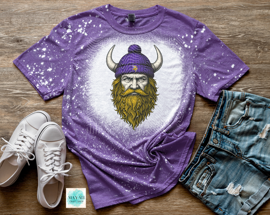 Purple t-shirt with a graphic of a bearded man in a Viking hat on a wooden surface with white sneakers and denim shorts.