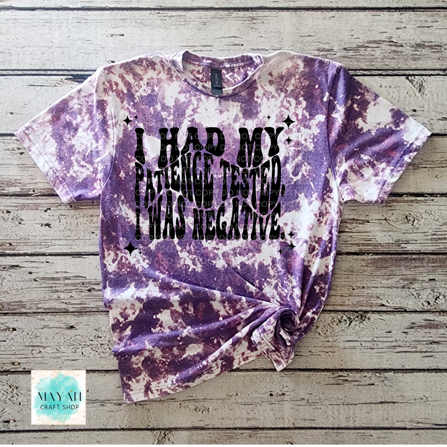 Purple tie-dye t-shirt with text on a wooden surface, featuring the brand 'Mayan Craft Shop'.