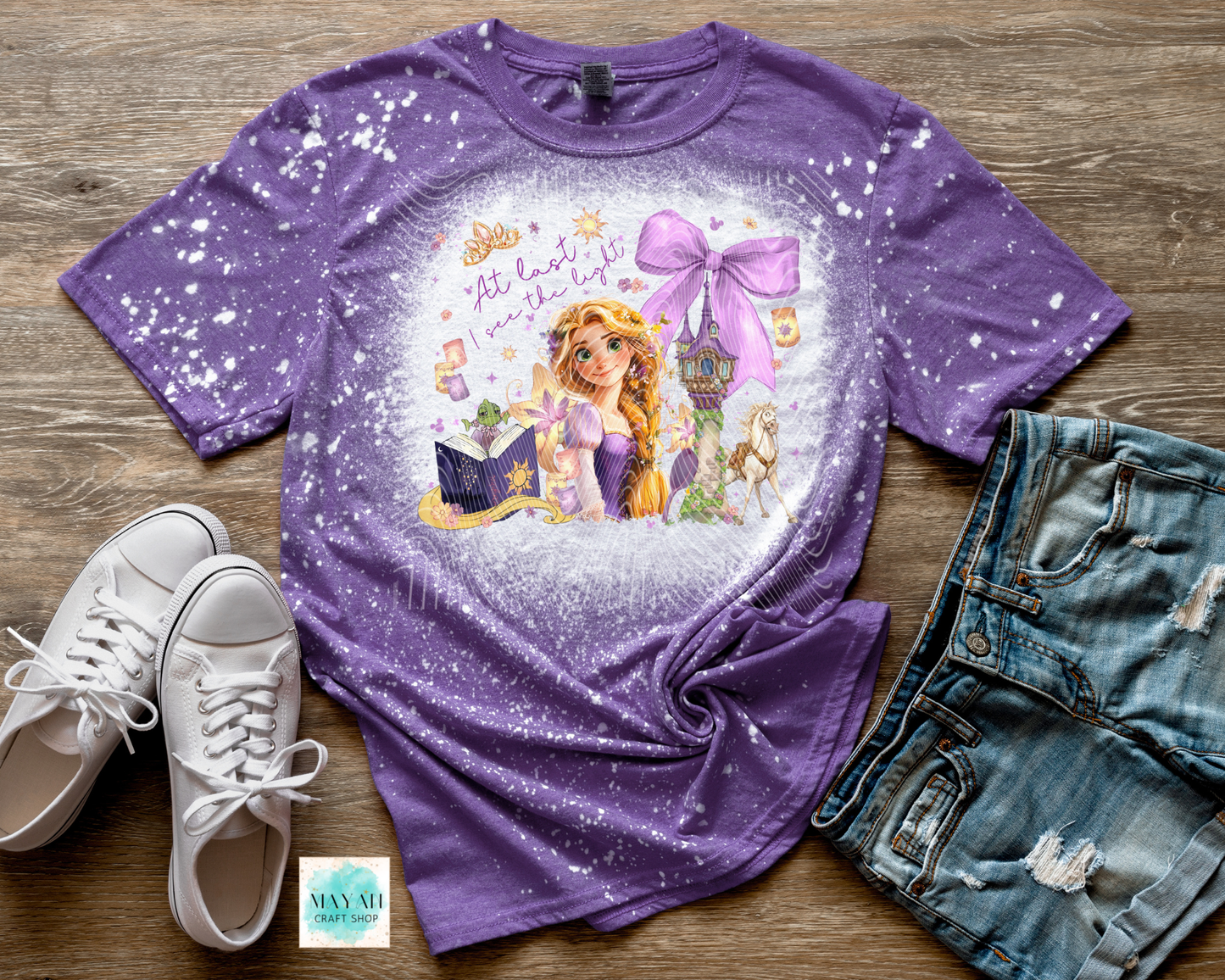 Purple t-shirt with princess graphic on a wooden surface with shoes and shorts.