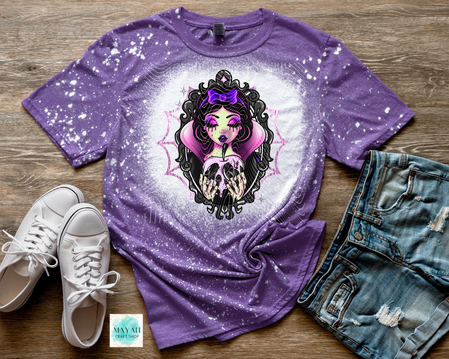 Purple t-shirt with graphic design on a wooden surface with shoes and jeans.