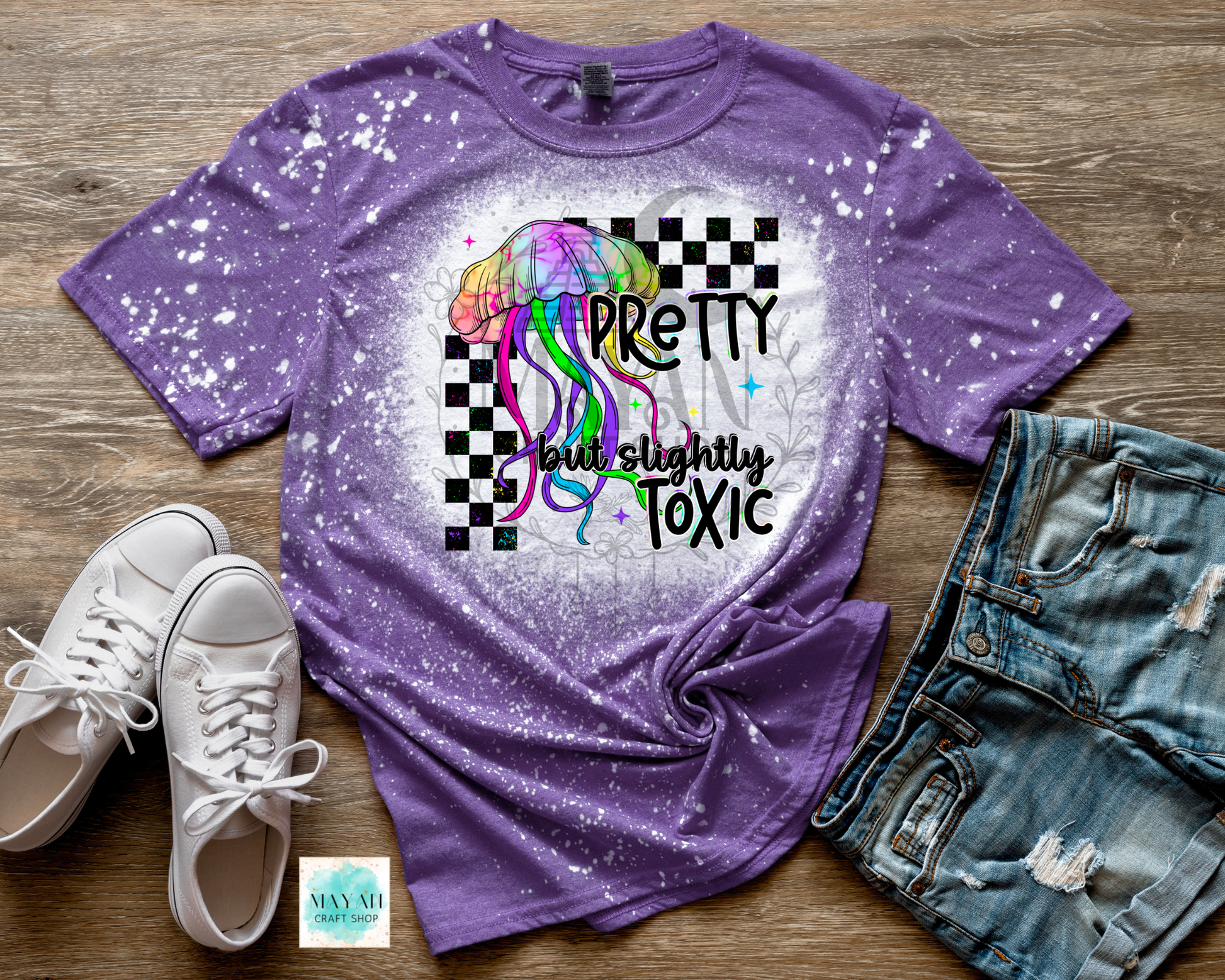 Purple t-shirt with colorful graphic and text on a wooden surface with shoes and jeans.