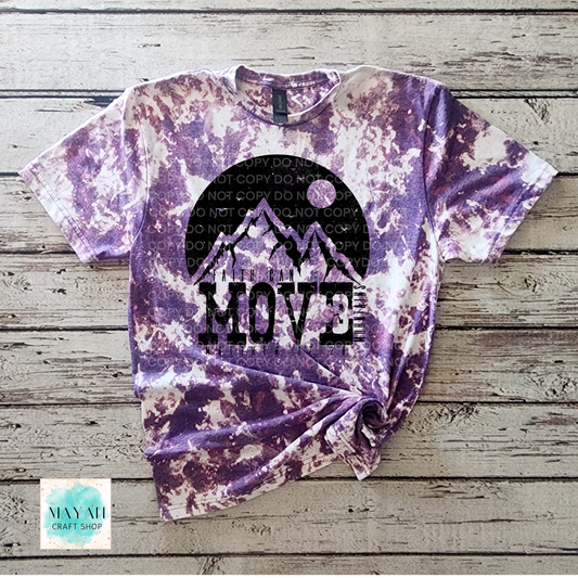 Tie-dye t-shirt with mountain design and 'MOVE' text on a wooden surface, featuring a watermark.