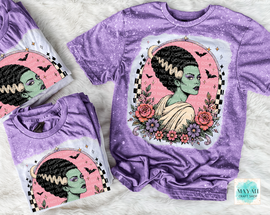 Purple t-shirt with a graphic design of a woman with green skin, flowers, and text on a white background.