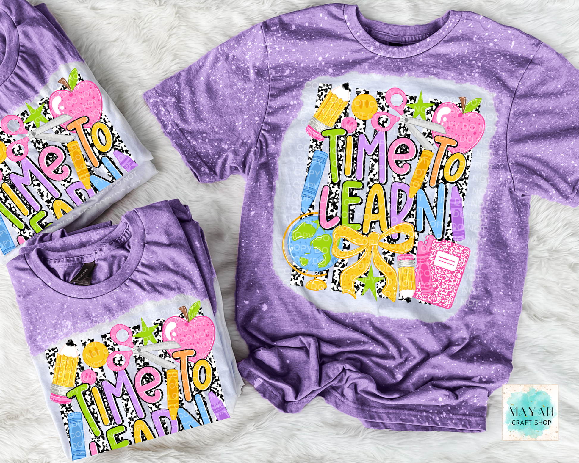 Three lavender short-sleeve graphic T-shirts arranged on a white faux-fur surface. The main shirt is laid flat and shows a large colorful front print reading “Time To Learn” with school-themed illustrations including apples, pencils, and a notebook.