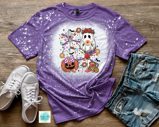 Purple t-shirt with a Halloween-themed design on a wooden surface with shoes and shorts.
