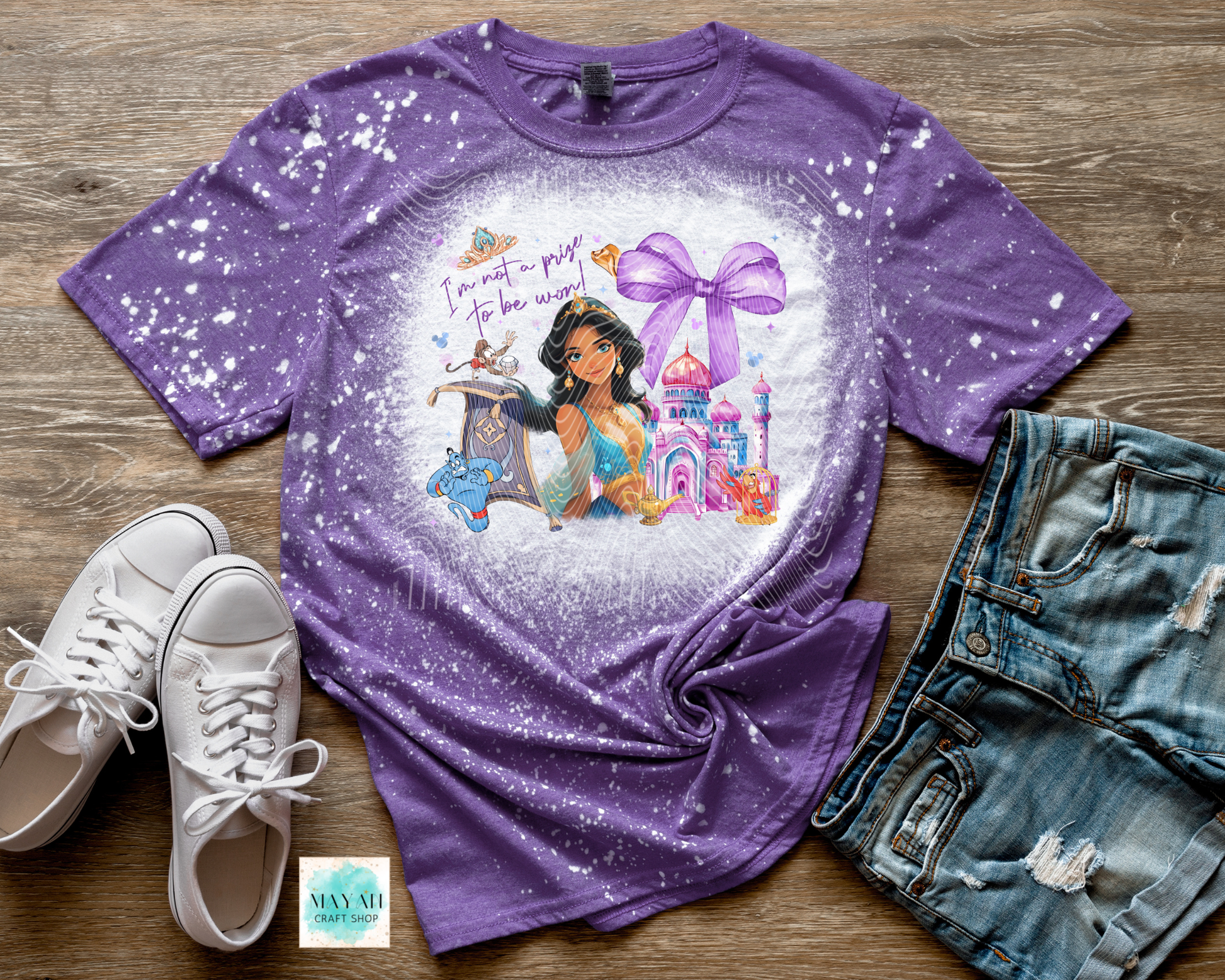Purple t-shirt with princess graphic and text on a wooden surface with shoes and shorts.
