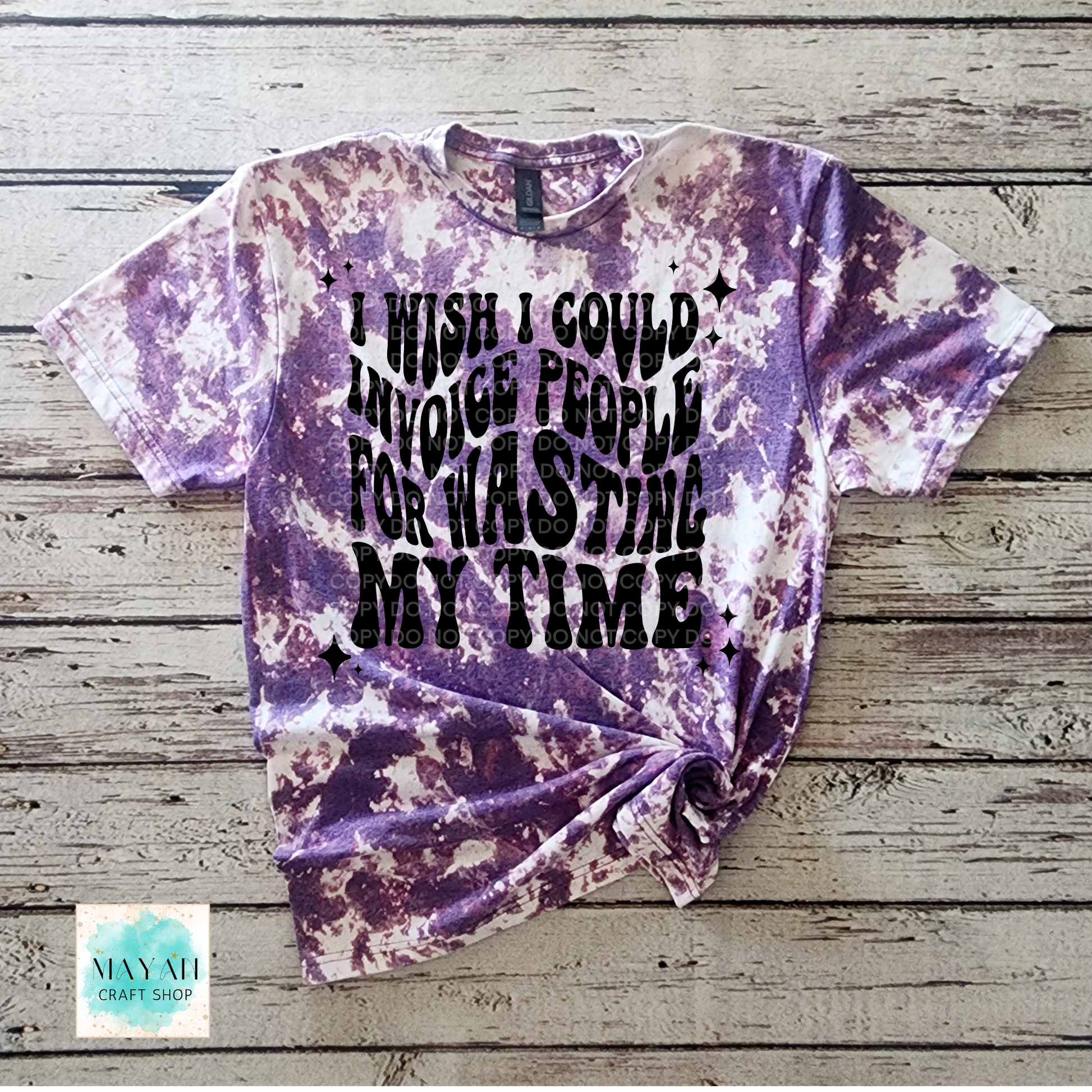 Purple tie-dye t-shirt with black text on a wooden surface, featuring the brand 'Mayan Craft Shop'.