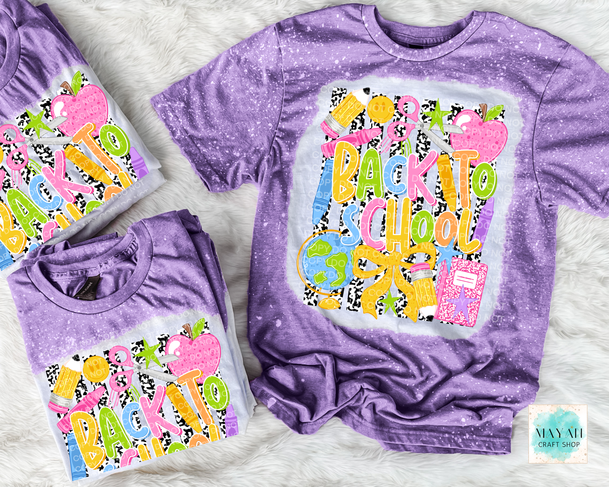 Three purple short-sleeve t-shirts with a colorful 'Back to School' graphic, arranged on a white faux fur background. The main shirt is laid flat, while two smaller shirts are folded.