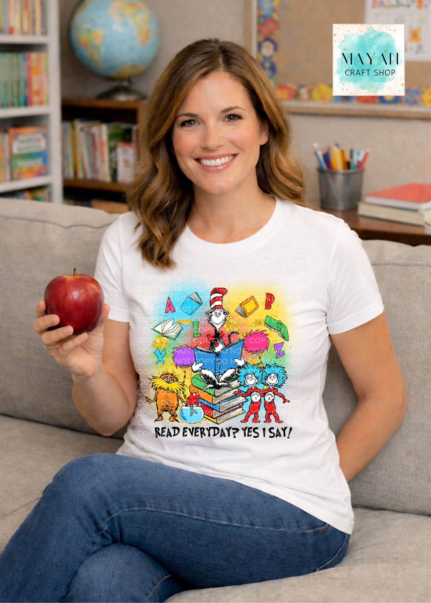 Woman wearing a white t-shirt with a colorful graphic design, holding an apple, sitting on a couch in a classroom setting.