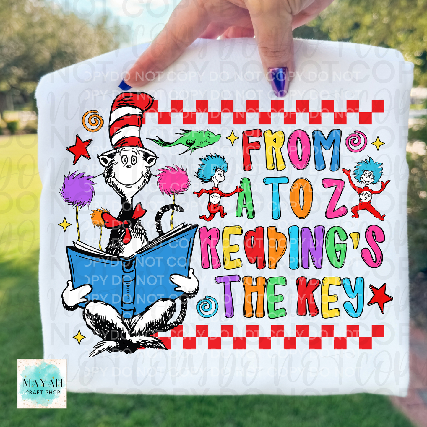 Shirt with colorful text and character design, held by a hand outdoors.