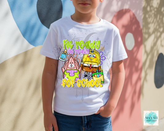 A child wearing a white graphic t-shirt featuring cartoon saying READY FOR SCHOOL' in yellow and green. The child is standing outdoors against a wall with painted shapes.