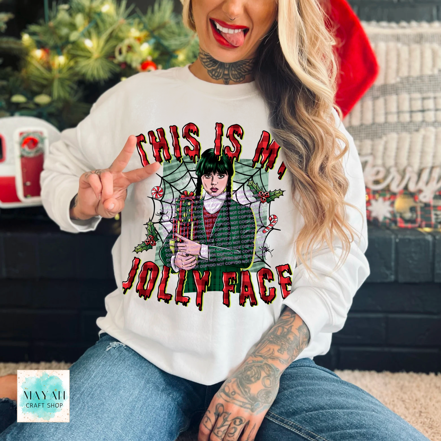 Person wearing a white sweatshirt with a Christmas-themed design and text, sitting in front of a decorated fireplace.