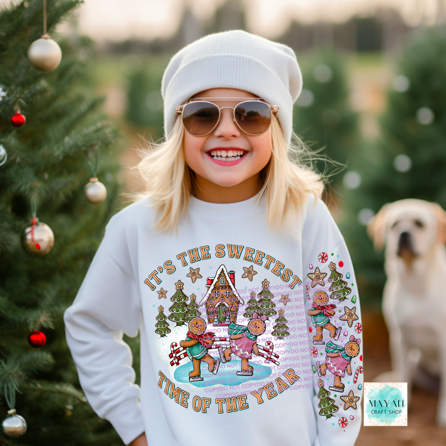 Child wearing a festive sweater with gingerbread men design, standing in front of Christmas trees.