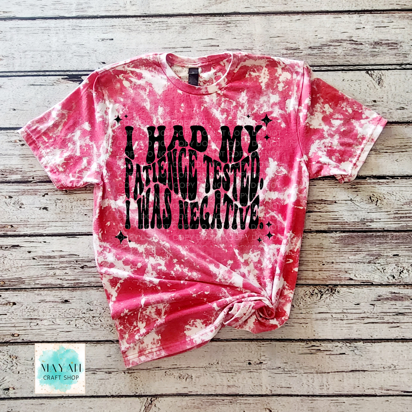 Pink tie-dye t-shirt with black text on a wooden surface, featuring the brand 'Mayan Craft Shop'.