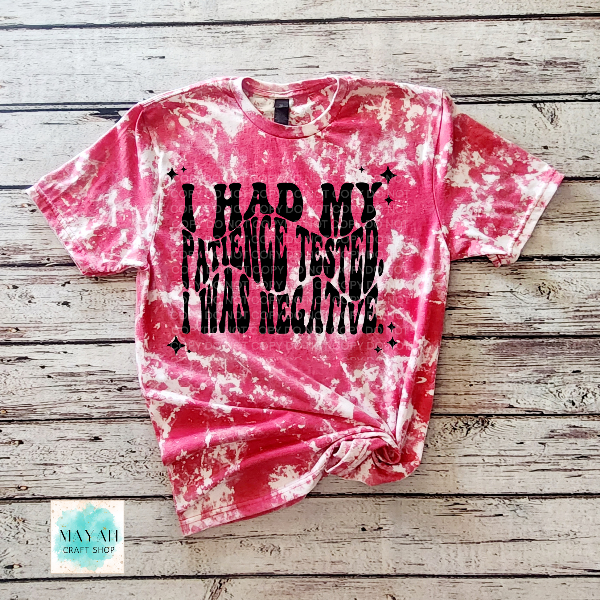Pink tie-dye t-shirt with black text on a wooden surface, featuring the brand 'Mayan Craft Shop'.