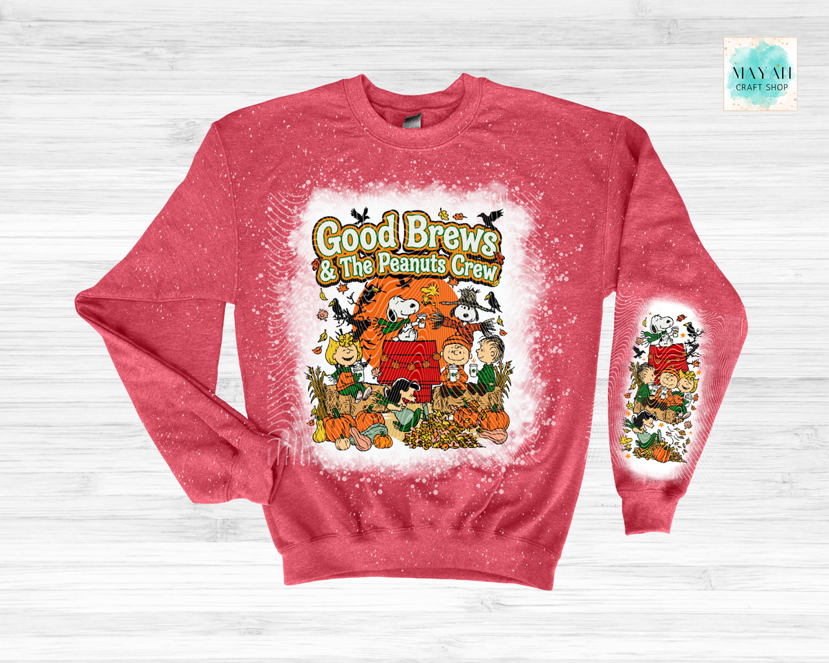 A heather red crewneck sweatshirt featuring a 'Good Brews' graphic on the front and sleeve, displayed on a light gray wood plank background.