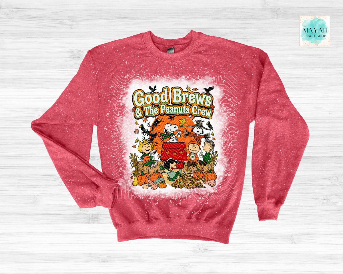 A heathered red crewneck sweatshirt featuring a 'Good Brews' graphic print on the front, displayed flat on a light gray wood background.