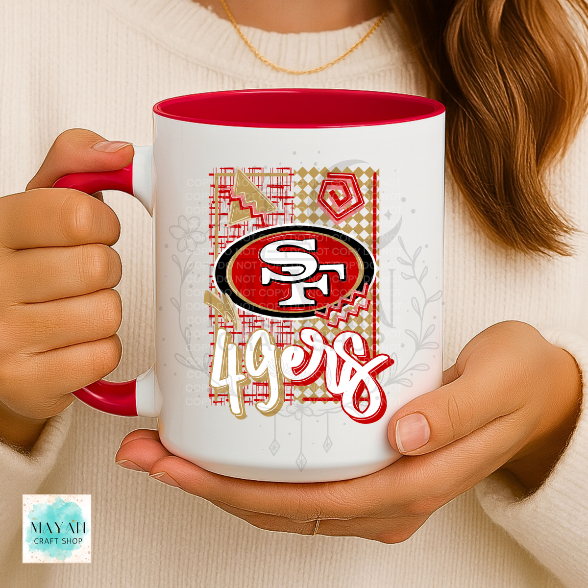 A person holding a white ceramic mug with a red interior and handle. The mug features a football team graphic with the team logo over a patterned background.