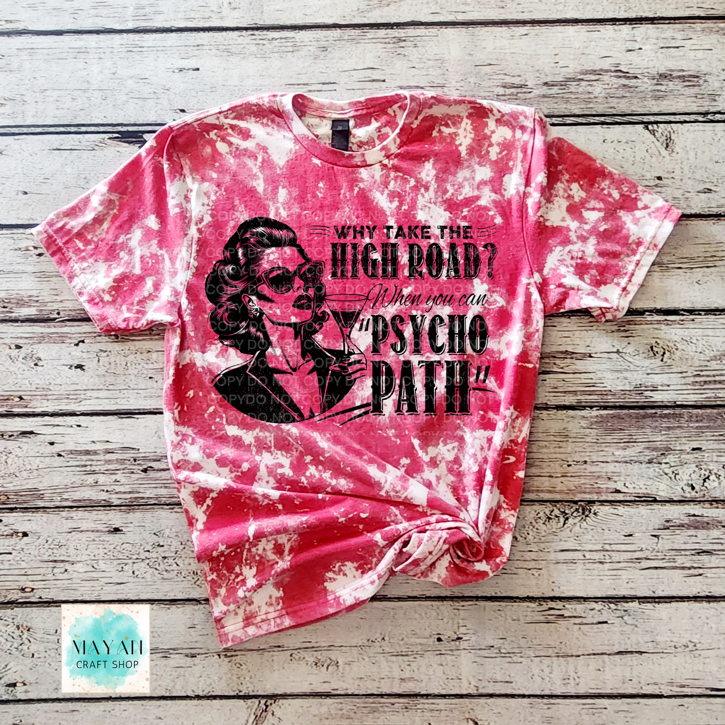Pink tie-dye t-shirt with graphic design and text on a wooden surface, brand 'Mayan Craft Shop'.