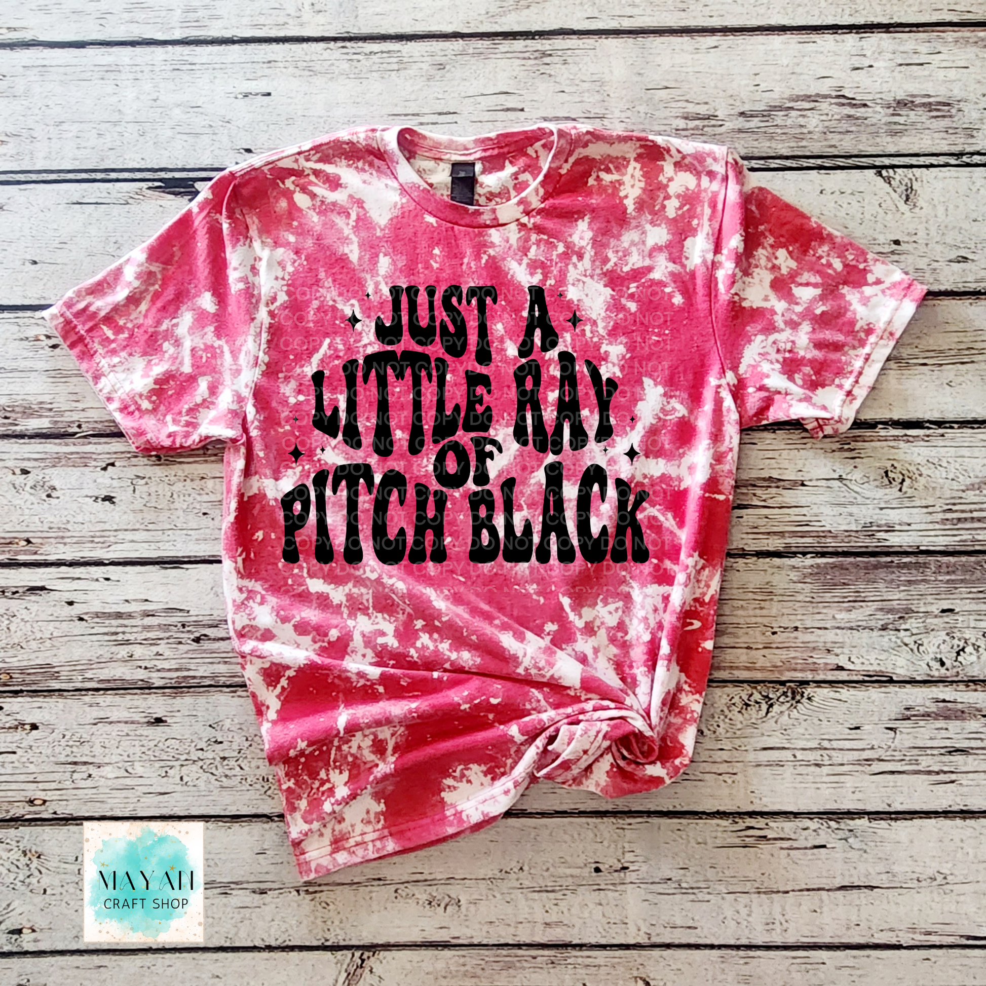 Pink tie-dye t-shirt with black text on a wooden surface, featuring the brand 'Mayan Craft Shop'.