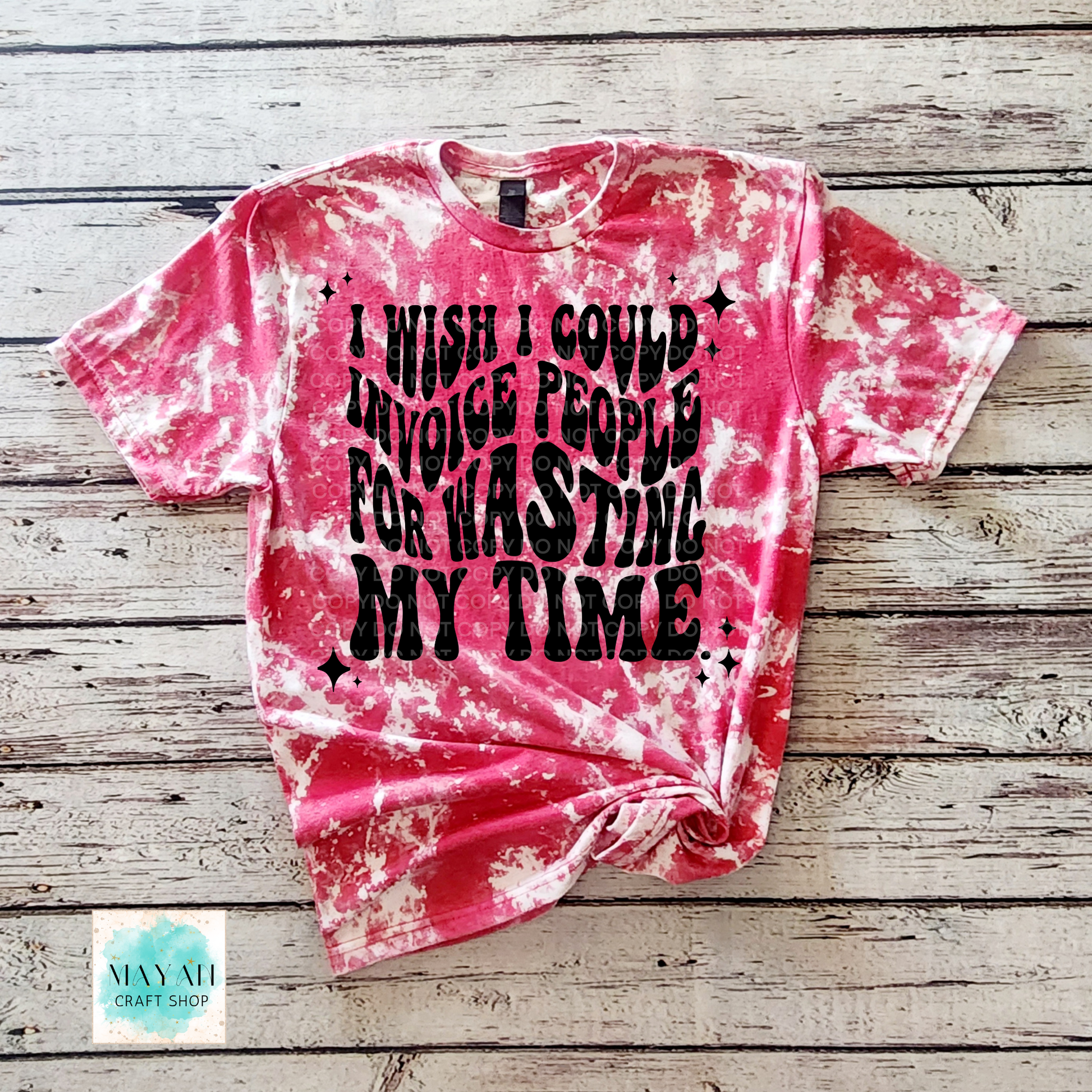 Pink tie-dye t-shirt with black text on a wooden surface, branded 'Mayan Craft Shop'.