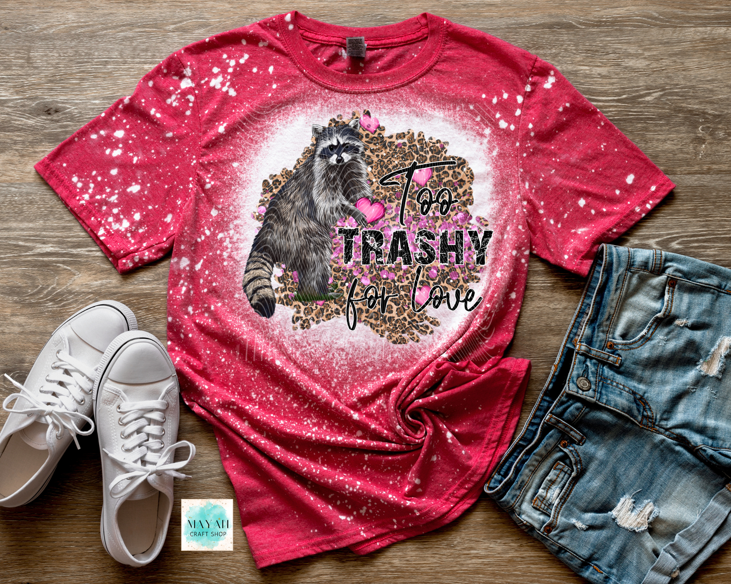 Red t-shirt with a raccoon graphic and text, paired with white sneakers and denim shorts on a wooden surface.