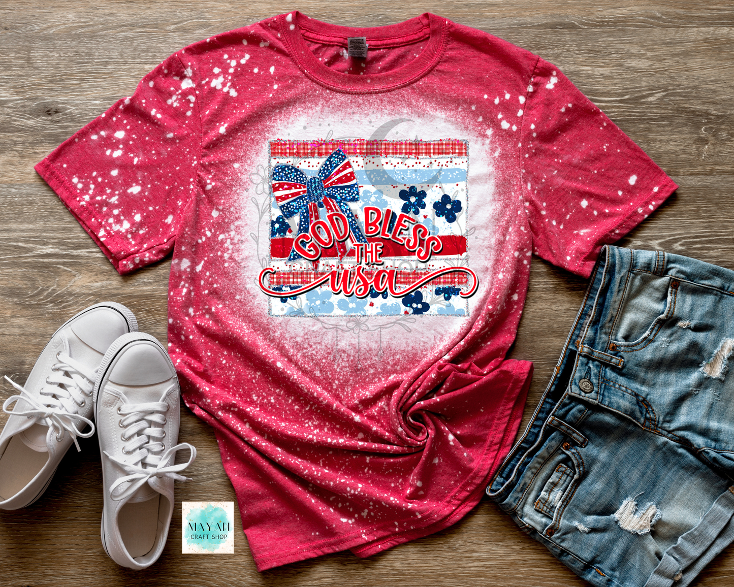 Red t-shirt with graphic design on a wooden surface with white sneakers and denim shorts.