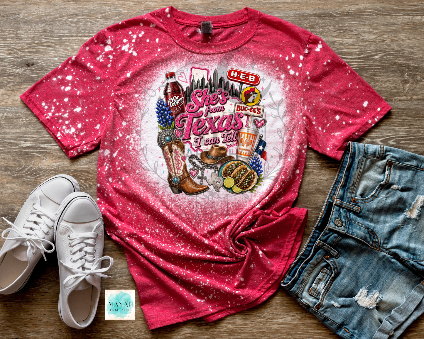 Red t-shirt with Texas-themed graphic on a wooden surface with white sneakers and denim shorts.
