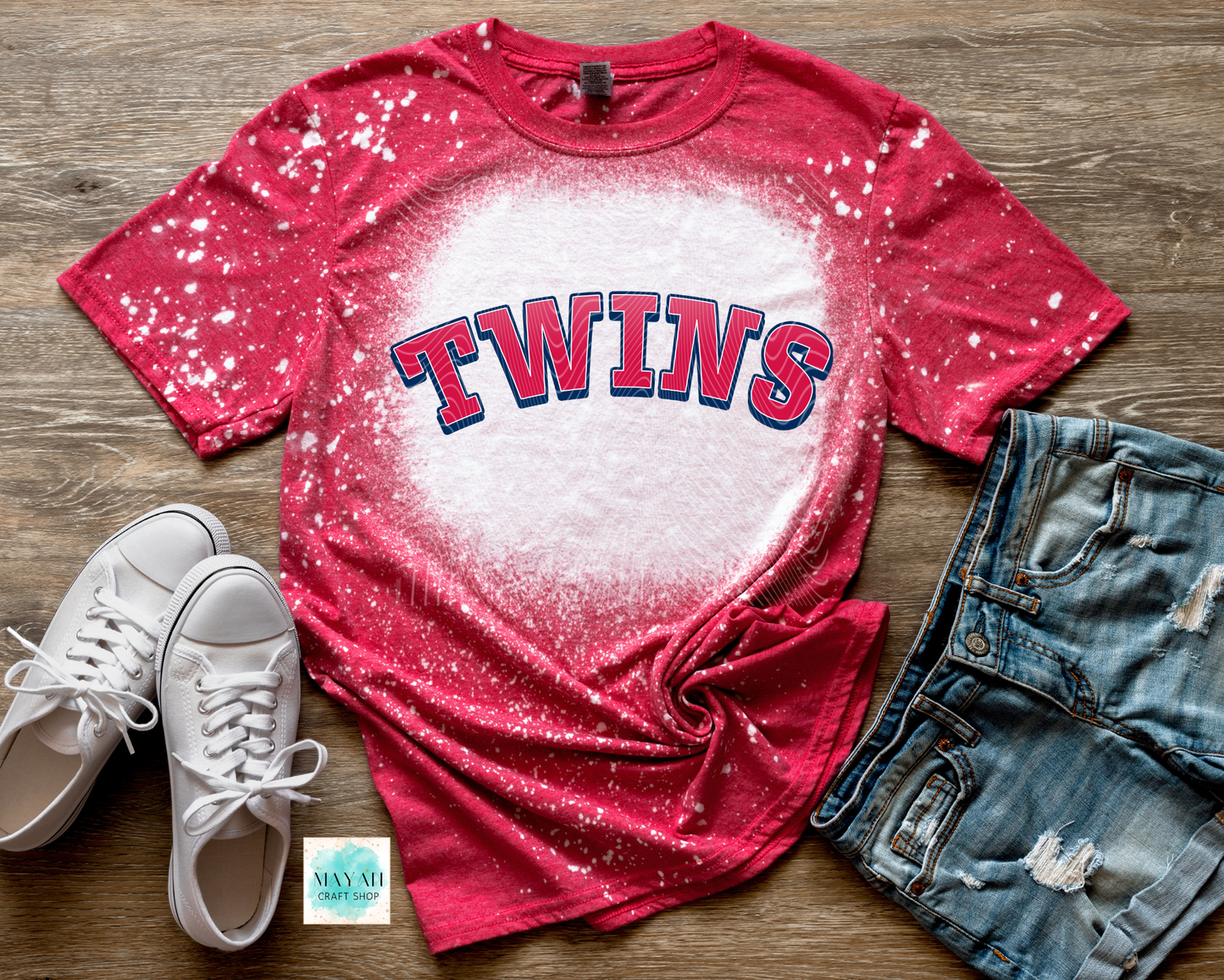 Red baseball t-shirt with white splatter design on a wooden surface, paired with white sneakers and denim shorts.
