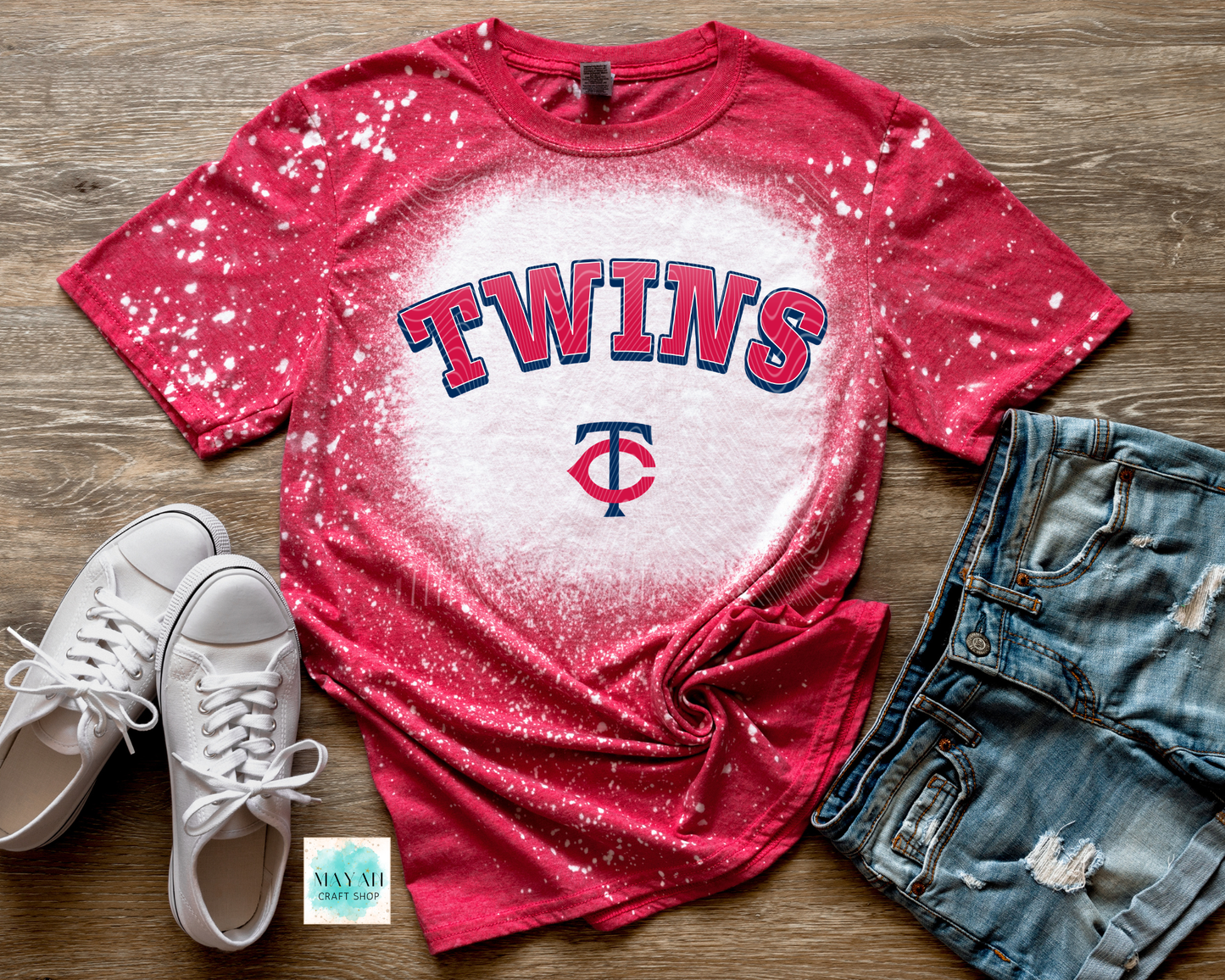 Red baseball t-shirt with white splatter design on a wooden surface, accompanied by white sneakers and denim shorts.
