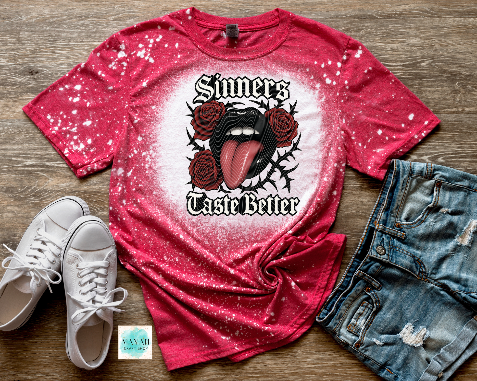Red t-shirt with graphic design on a wooden surface with white sneakers and denim shorts.