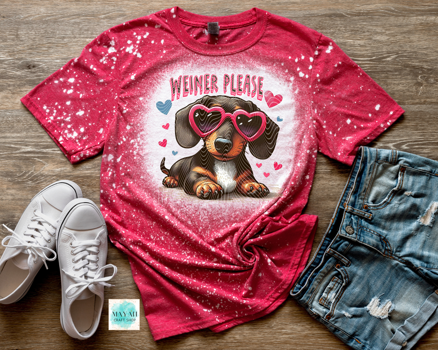 Red t-shirt with a dachshund graphic and 'Weiner Please' text on a wooden surface with white sneakers and denim shorts.