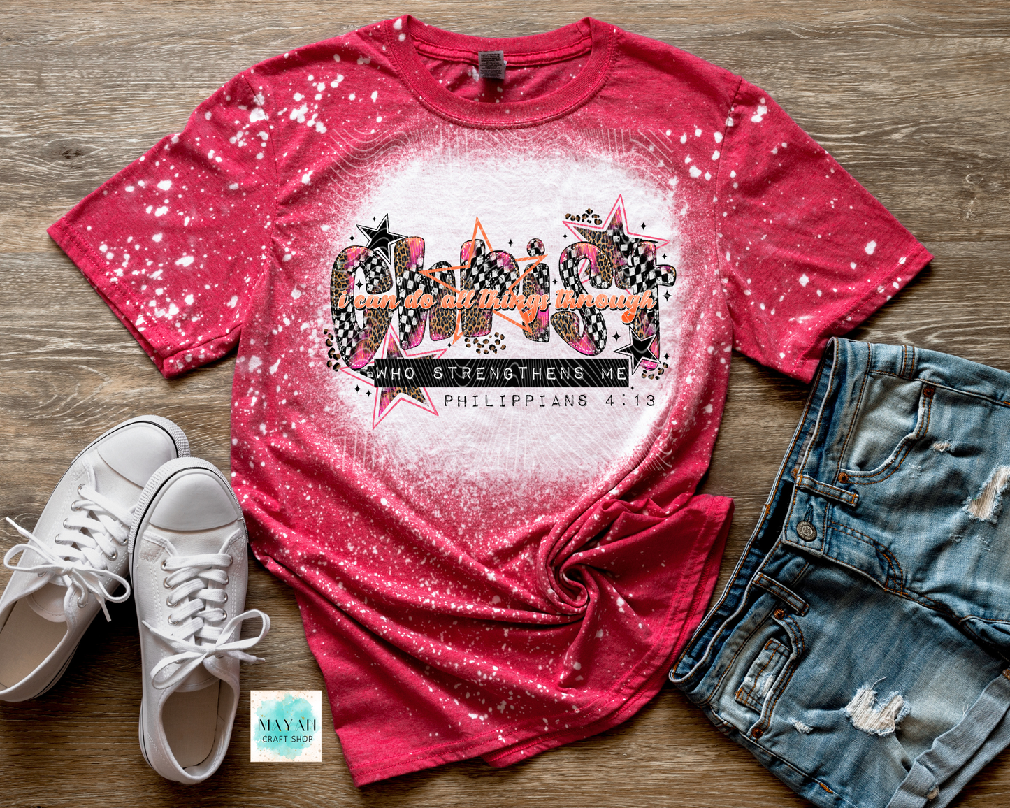 Red bleached t-shirt with graphic design, white sneakers, and denim shorts on a wooden surface.