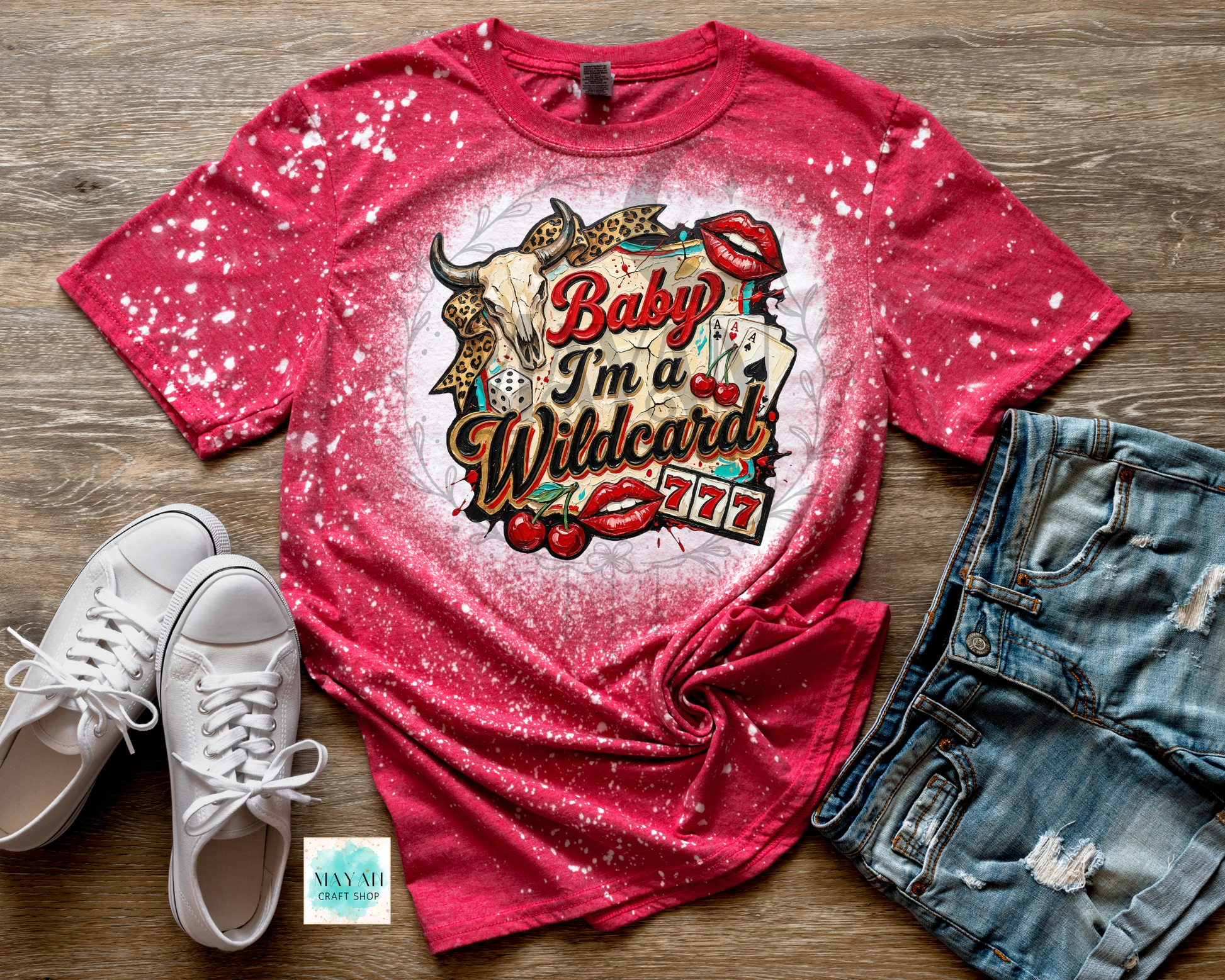 Red graphic t-shirt with 'I'm a Wildcard' design on a wooden surface with white sneakers and denim shorts.