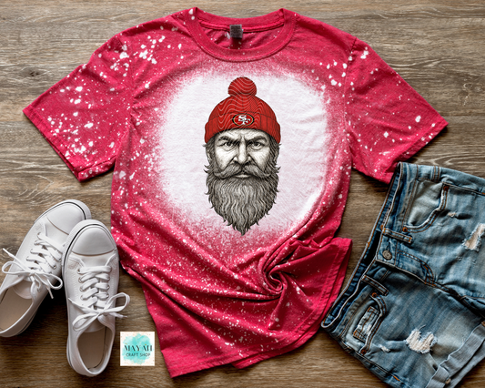 Red t-shirt with graphic design of a bearded man wearing a red beanie, paired with white sneakers and denim shorts on a wooden surface.