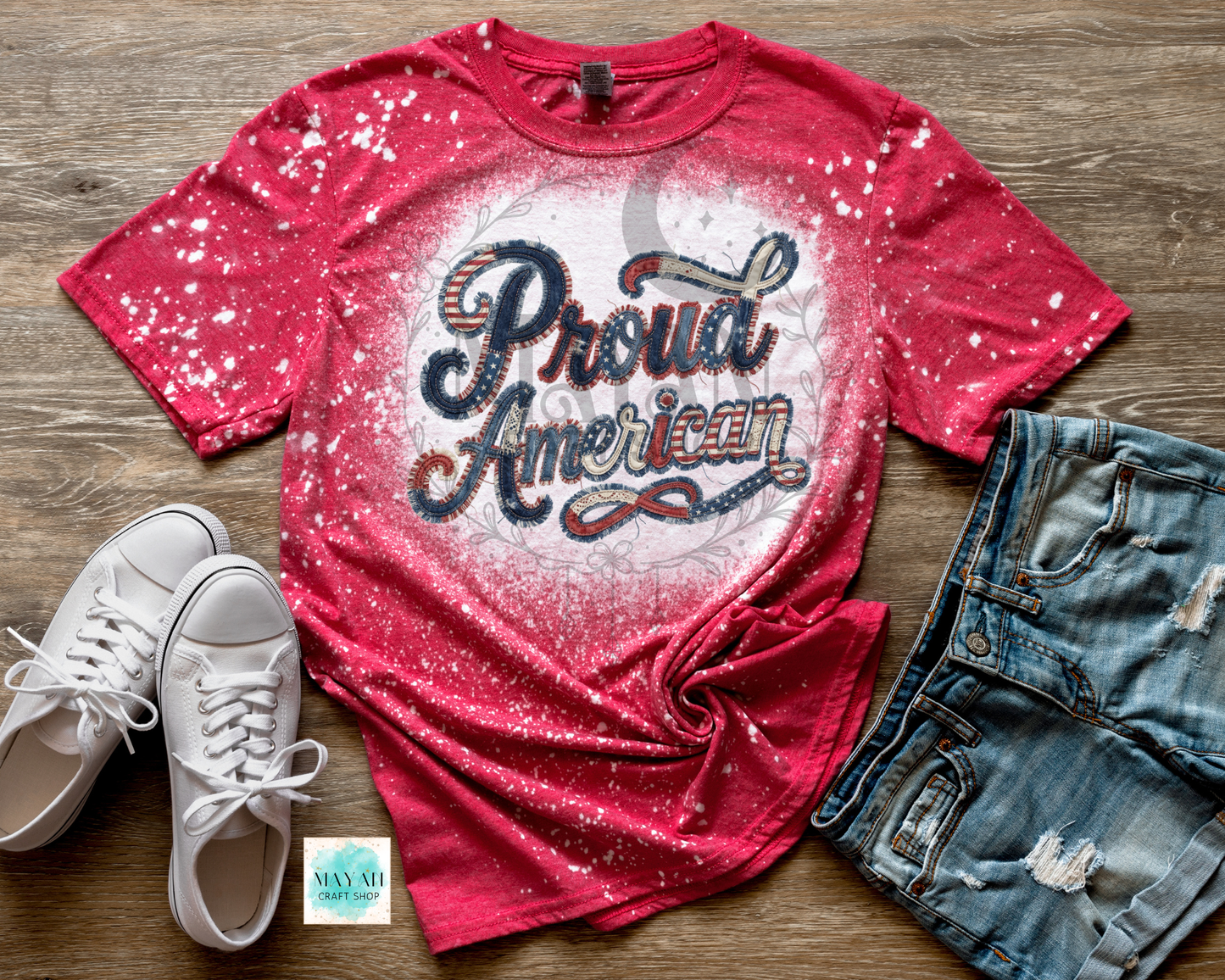 Red t-shirt with 'Proud American' text, white sneakers, and denim shorts on a wooden surface.