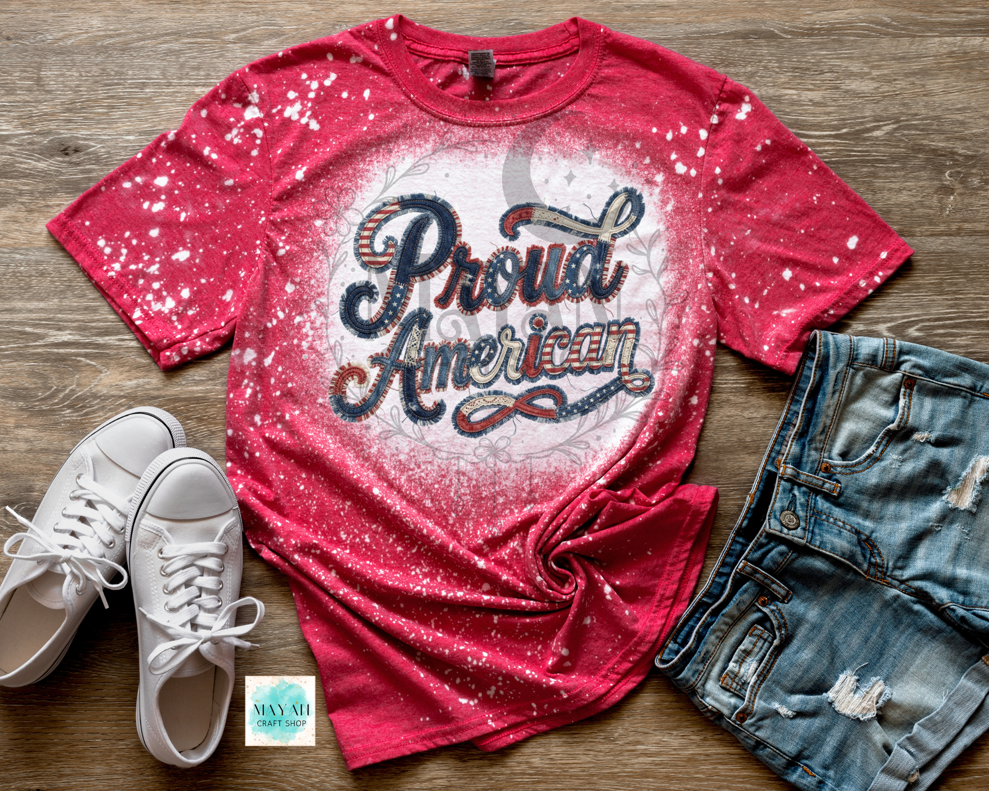 Red t-shirt with 'Proud American' text, white sneakers, and denim shorts on a wooden surface.