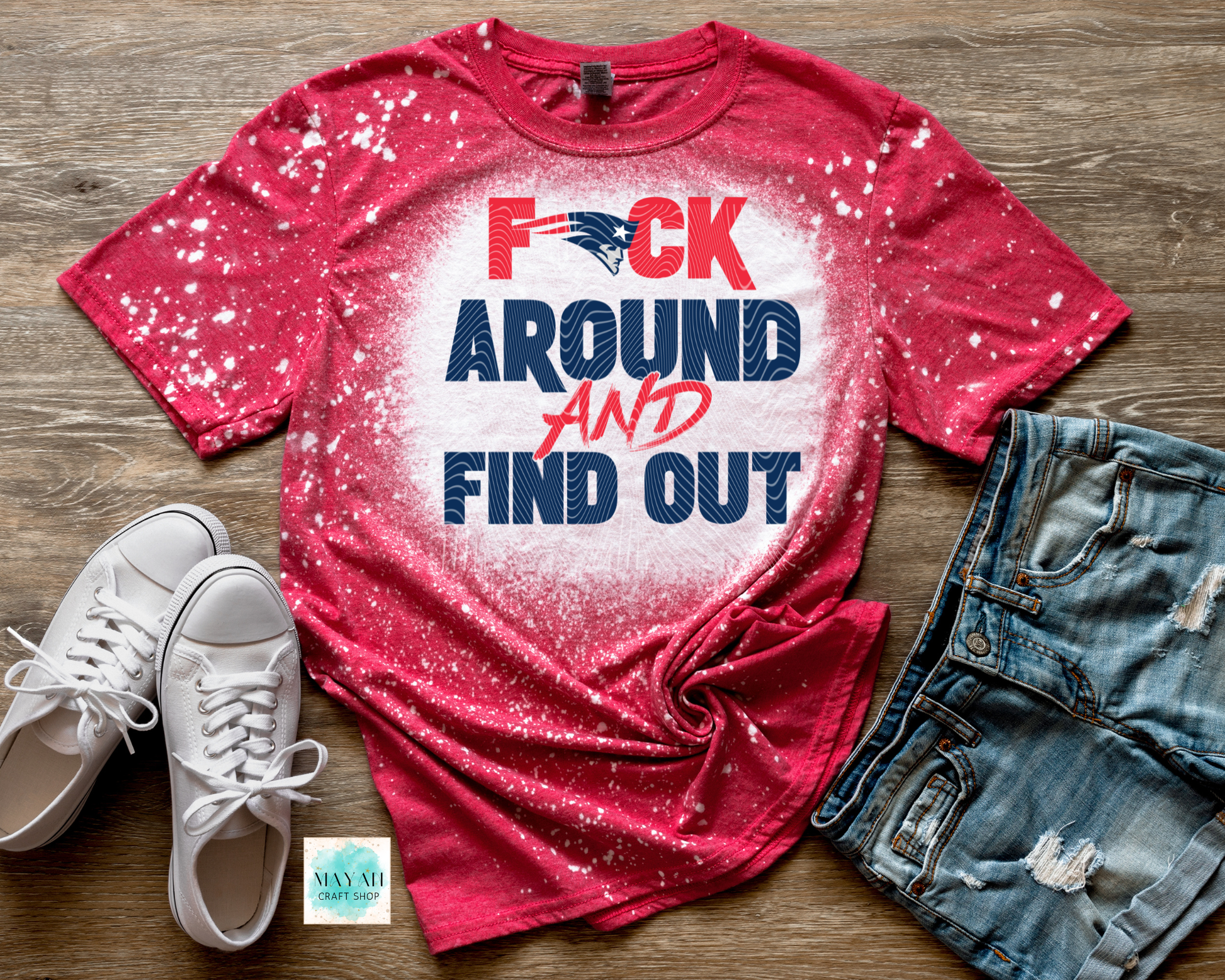 Red t-shirt with graphic text, white sneakers, and denim shorts on a wooden surface