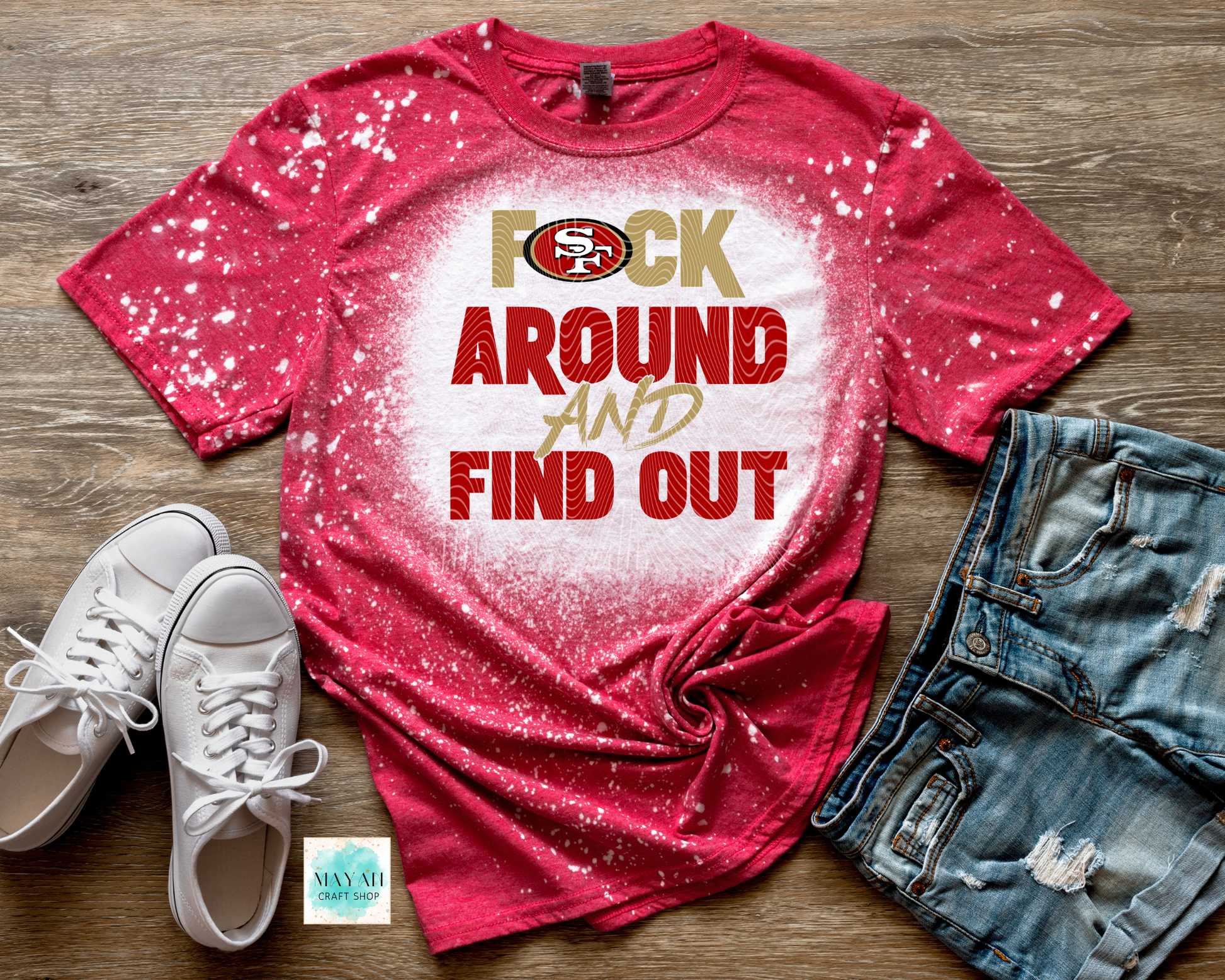 Red t-shirt with text and logo, white sneakers, and denim shorts on a wooden surface