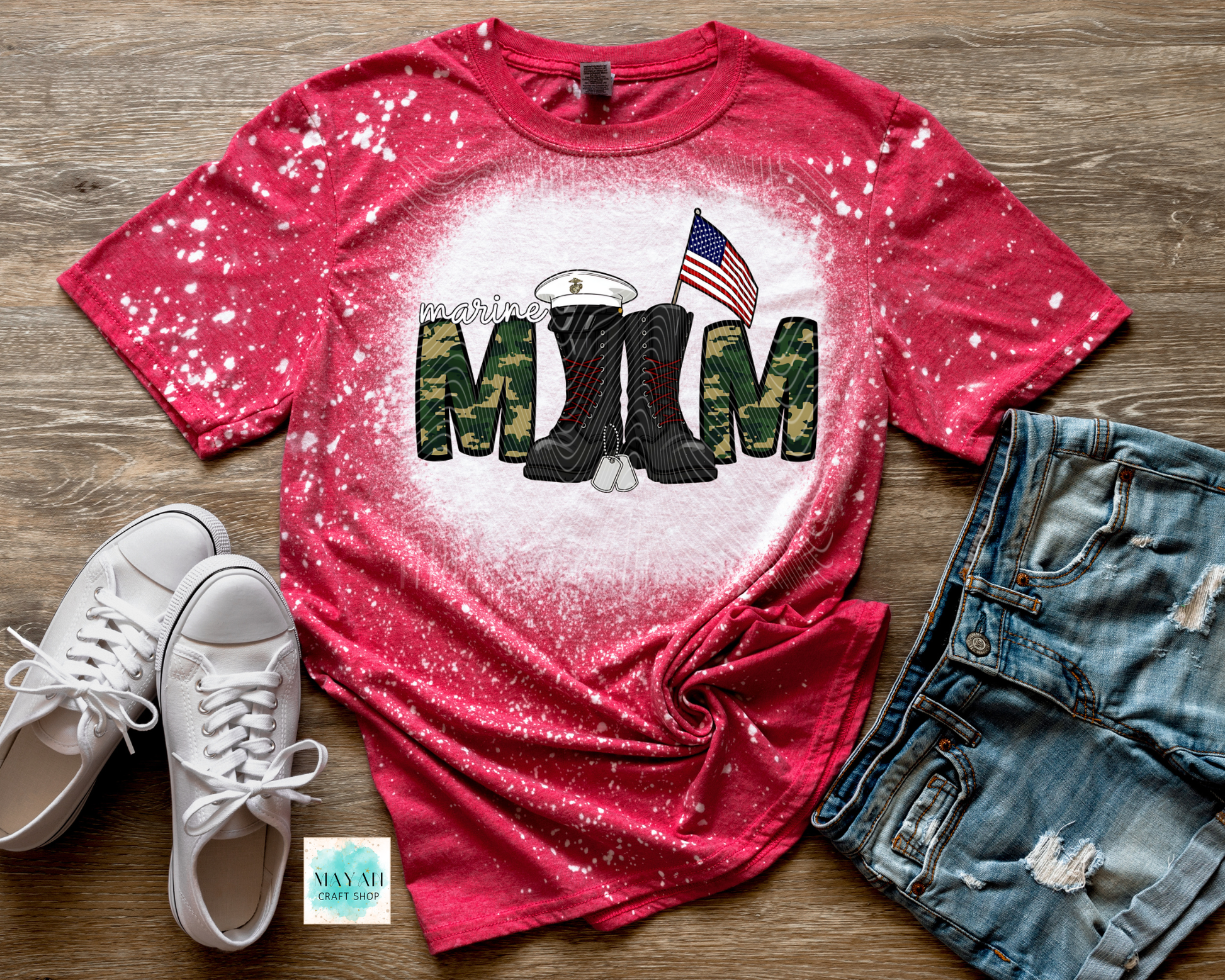 Red t-shirt with military mom design featuring boots and an American flag, paired with white sneakers and denim shorts on a wooden surface.