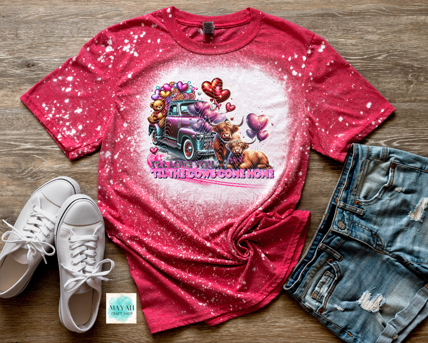 Red t-shirt with graphic design on a wooden surface with white sneakers and denim shorts.