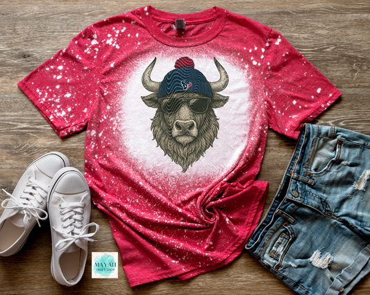 Red t-shirt with a bull graphic wearing a cap, paired with white sneakers and denim shorts on a wooden surface.