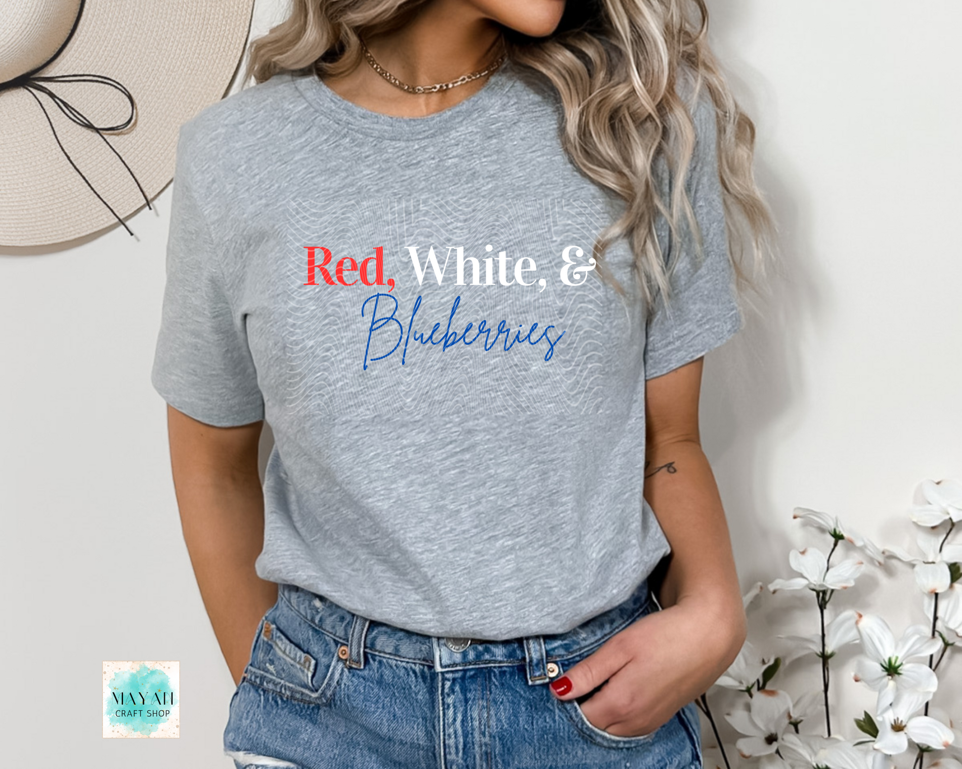 Person wearing a gray t-shirt with 'Red, White & Blueberries' text, standing against a light background with flowers.