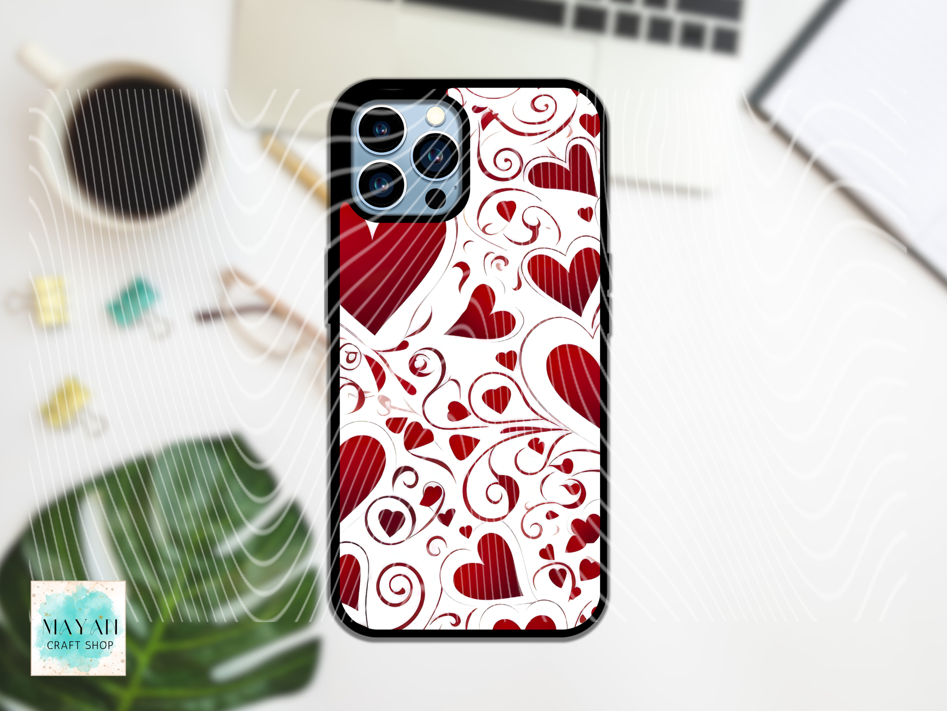 Phone case with red heart pattern on a white background, surrounded by office supplies.